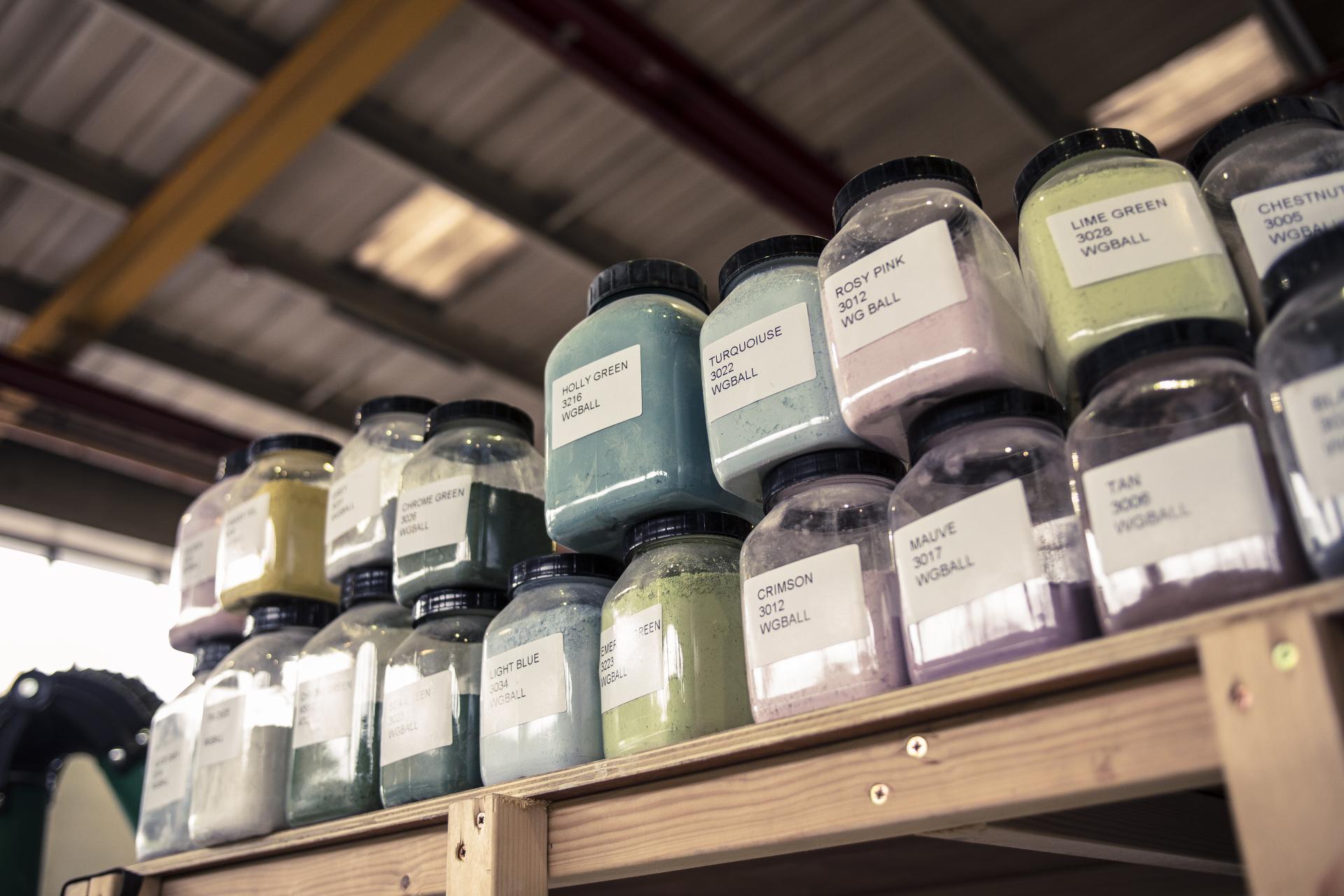 Colorful jars of sustainable materials are neatly arranged on shelves, showcasing Alusid's innovative palette for eco-friendly surfaces.