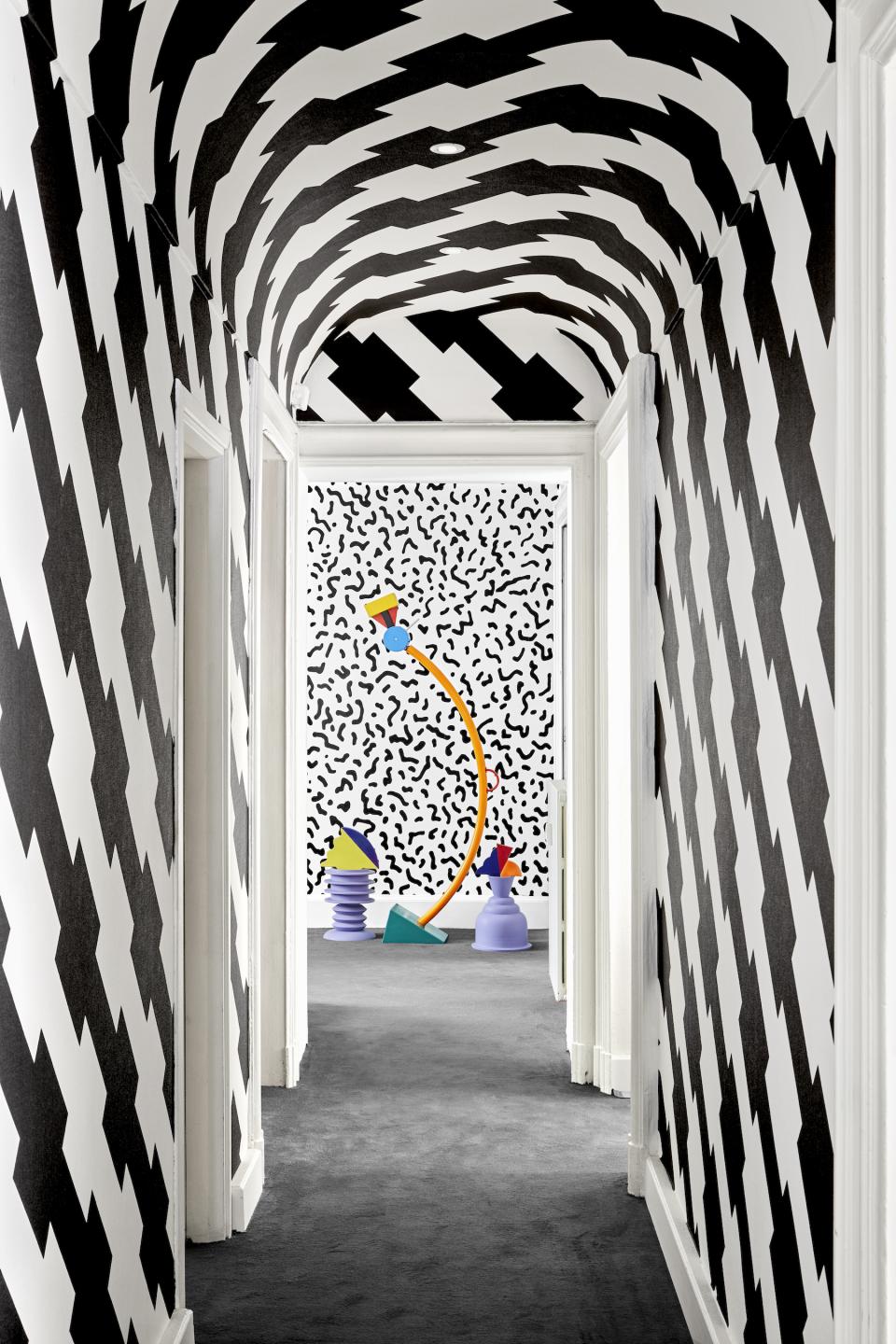 Bold black and white patterned walls frame a colorful Memphis Milano-inspired installation at the Post Design Gallery in Brera.
