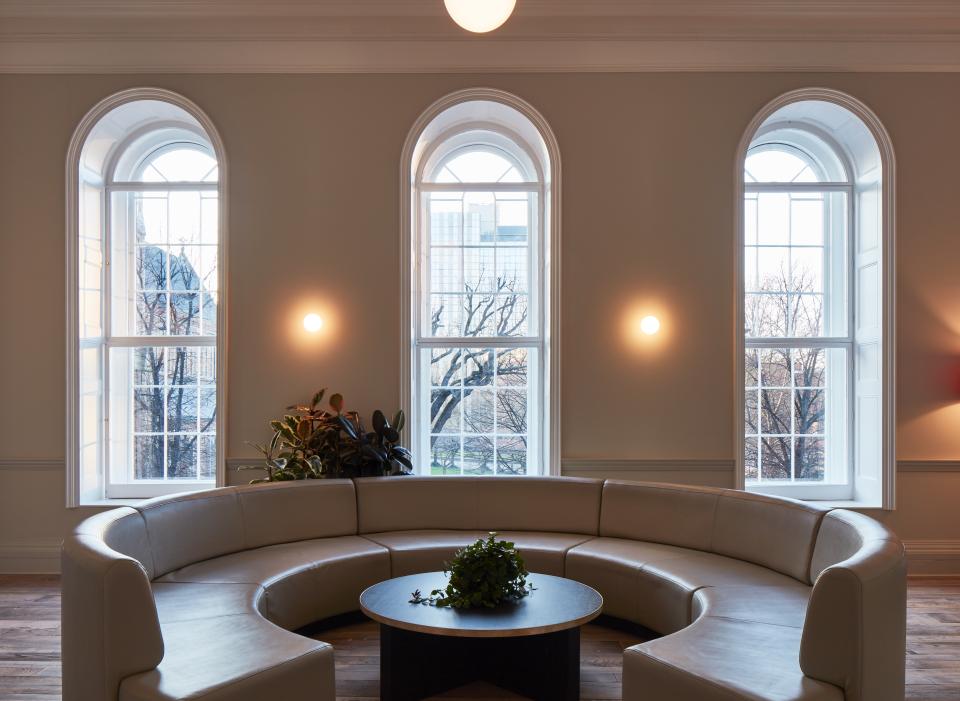 Elegant co-working space inspired by cocktail bars, featuring a circular sofa, plants, and natural light through large windows.