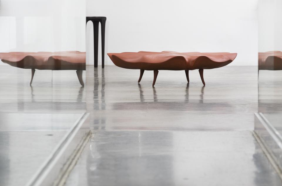 Sculptural wooden coffee table with organic curves, showcased in an art gallery featuring contemporary furniture design.