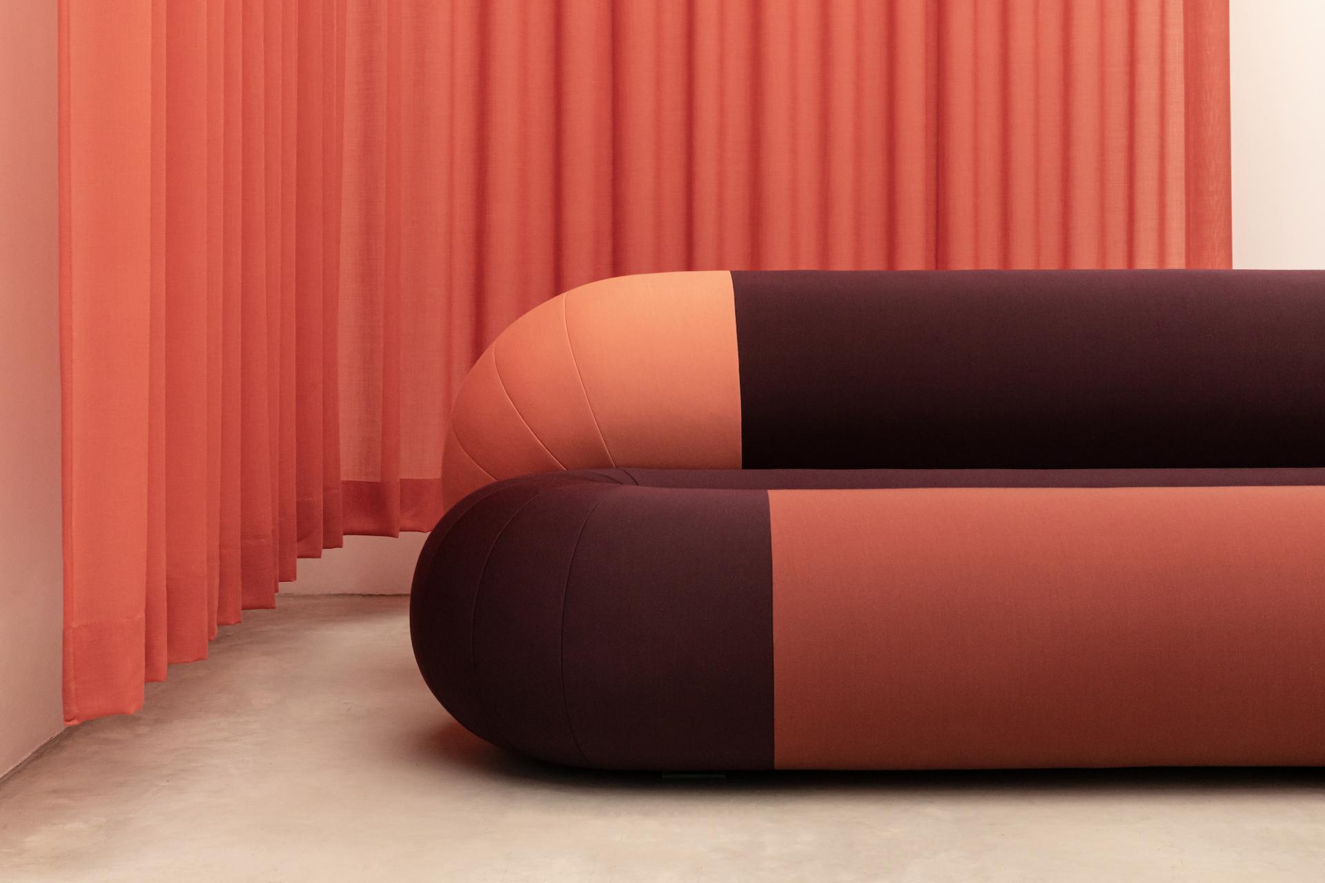 Modern furniture with bold, rounded shapes and rich, contrasting colors of burgundy and peach against a soft, draped background.