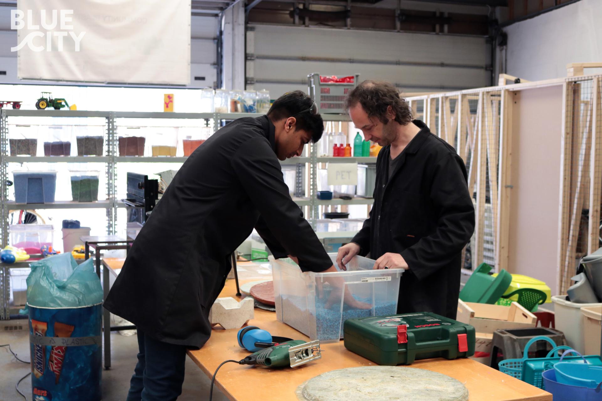 Two individuals work together with plastic waste materials, demonstrating sustainable design practices for affordable housing solutions.