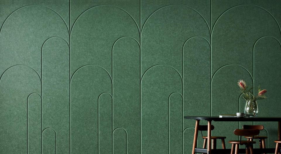 Modern green wall design with curved patterns, accompanied by a minimalist table and vase, showcasing innovative workspace aesthetics.