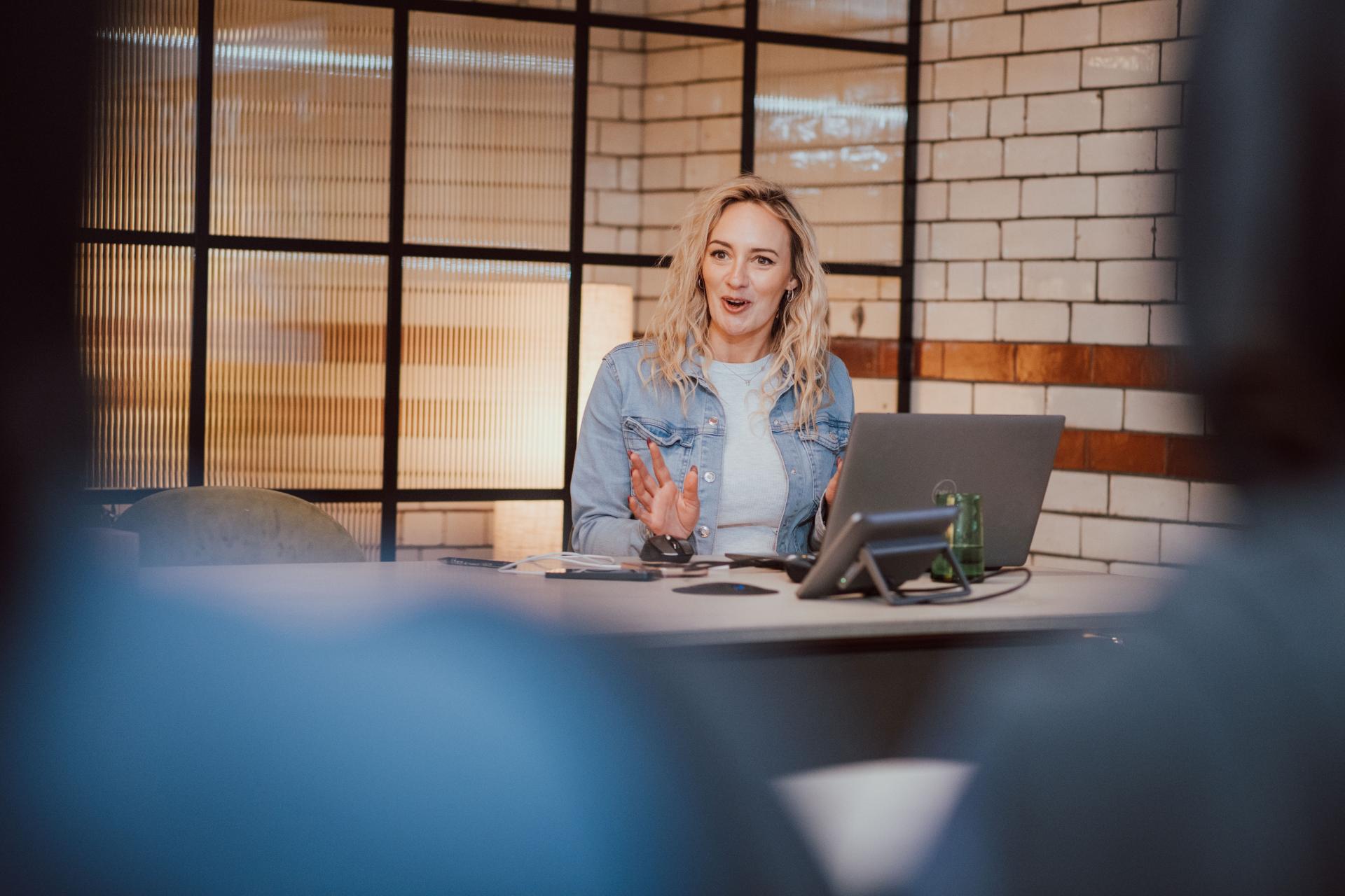 A woman in a denim jacket discusses interior design concepts in a creative workspace, engaging with her audience.