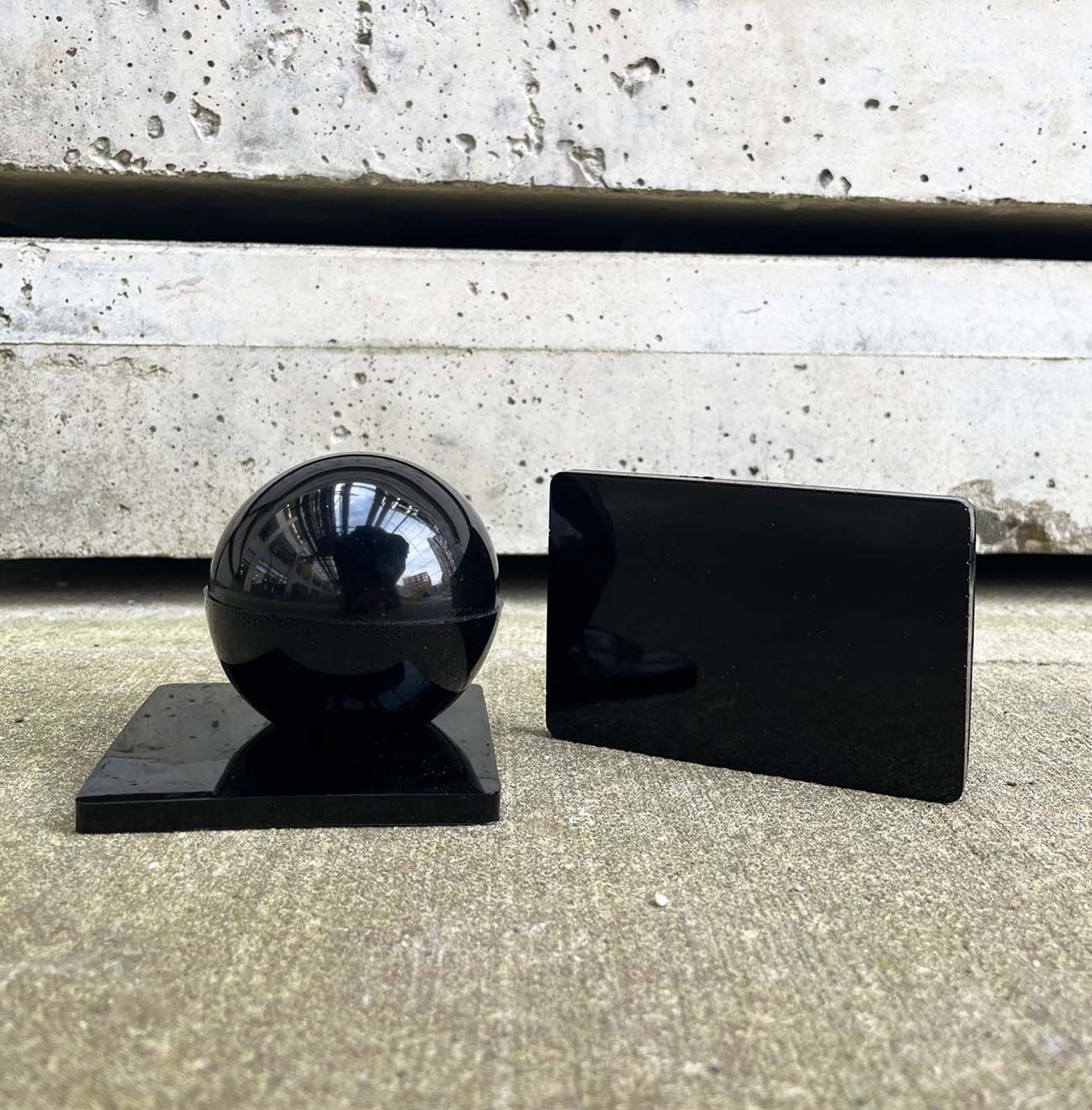 A reflective black sphere on a square base next to a glossy black rectangular block, showcasing sustainable design elements.