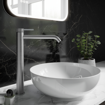 Sleek brassware faucet beside a glossy white vessel sink on a marble countertop, complemented by a modern plant and illuminated mirror.