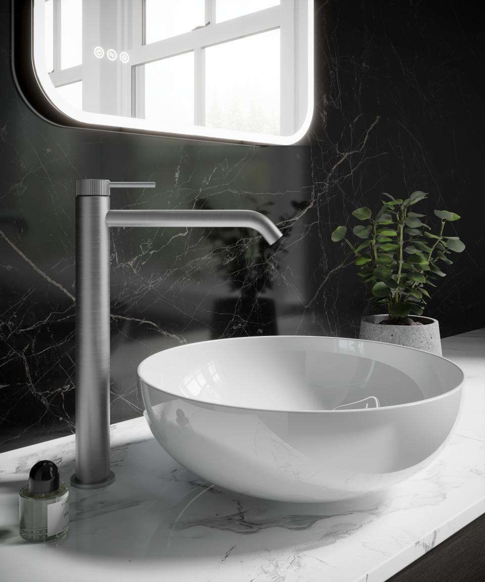 Sleek brassware faucet beside a glossy white vessel sink on a marble countertop, complemented by a modern plant and illuminated mirror.