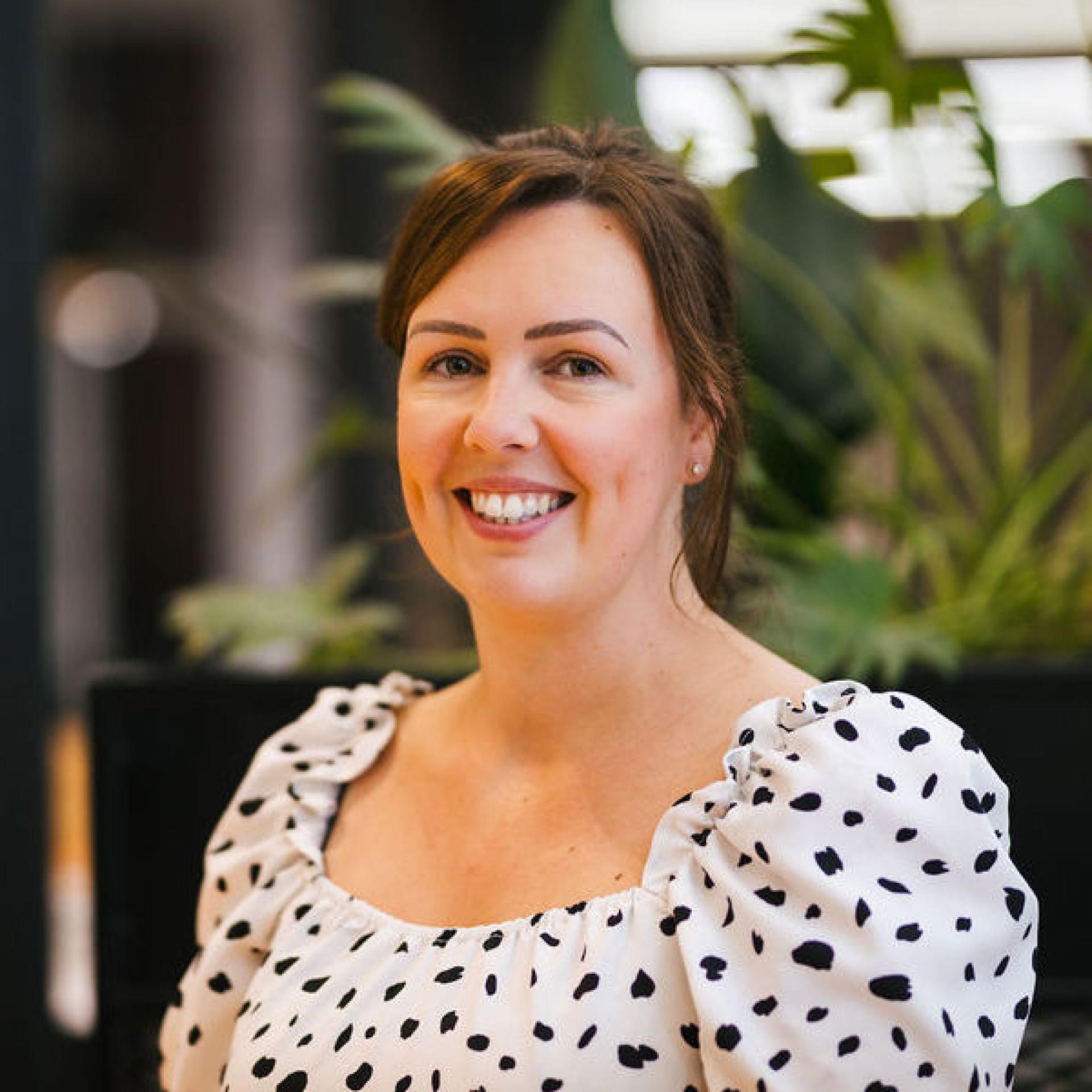 Professional woman smiling against a backdrop of greenery, representing discussions on Glasgow's property outlook and future trends.