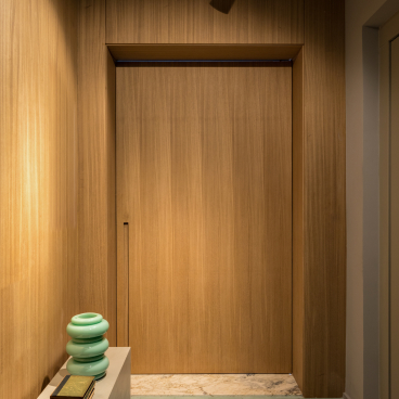 Modern apartment entryway in São Paulo featuring sleek wooden accents, a green vase, and stylish footwear on the floor.