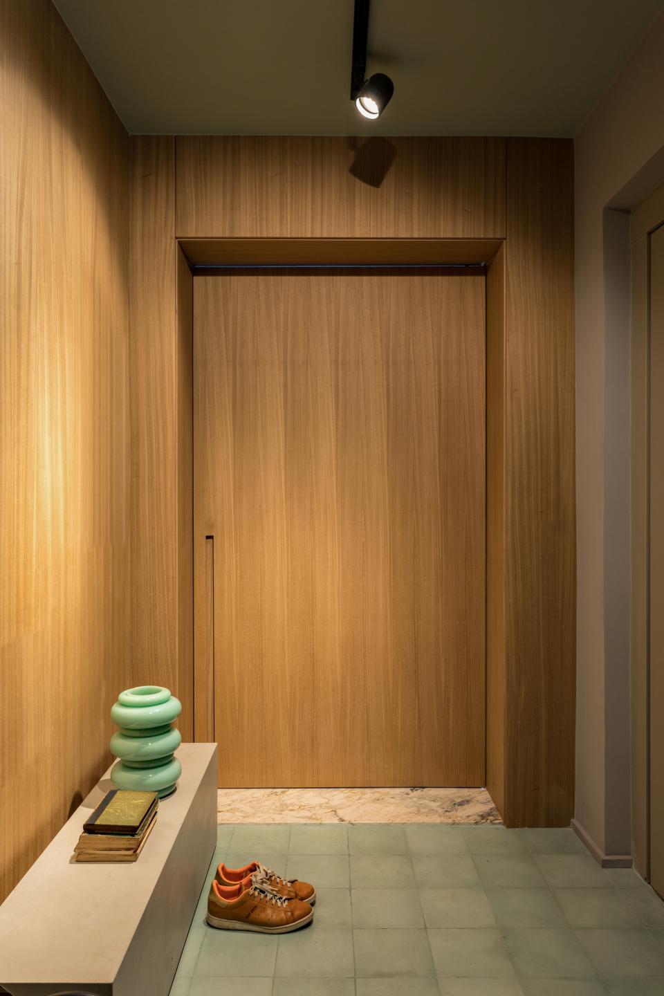 Modern apartment entryway in São Paulo featuring sleek wooden accents, a green vase, and stylish footwear on the floor.