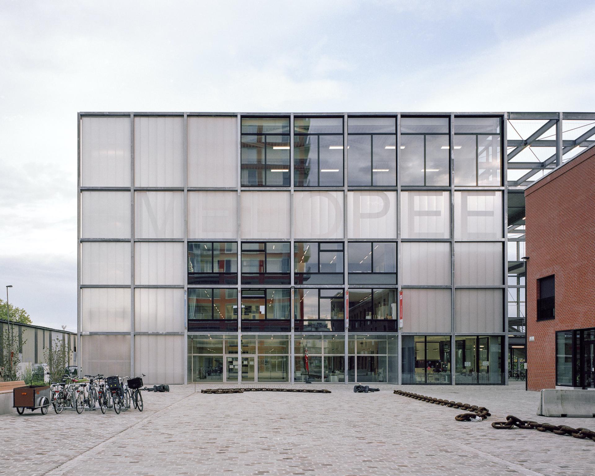 Modern multipurpose school building by Xaveer De Geyter Architects, featuring glass facade and bike parking in the harbour area.
