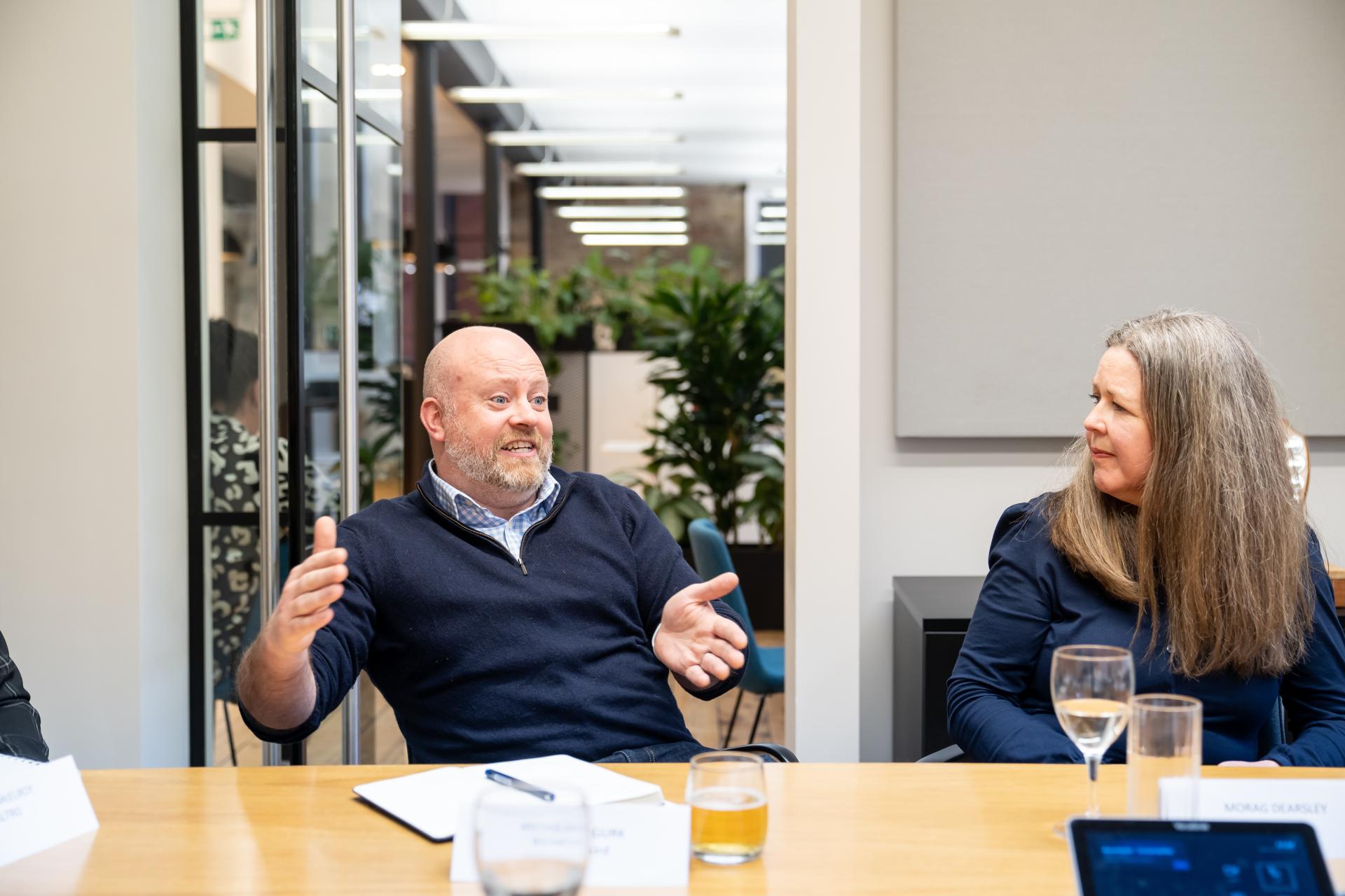 Participants engage in a discussion about sustainability initiatives in a modern office setting with greenery visible in the background.