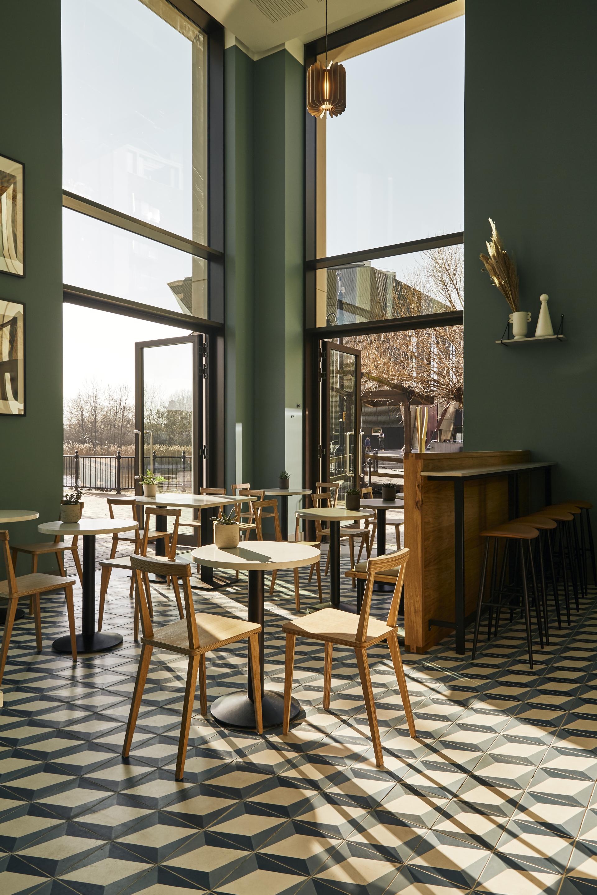Stylish coffee shop interior featuring Caesarstone Raw Concrete and Misty Carrera surfaces, with ample natural light and geometric flooring.