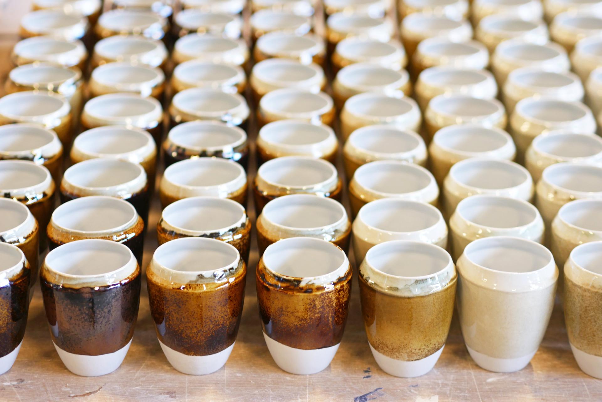 Handcrafted ceramic cups in various earthy colors, showcasing Agnė Kučerenkaitė’s innovative approach to sustainable design and waste re-identification.