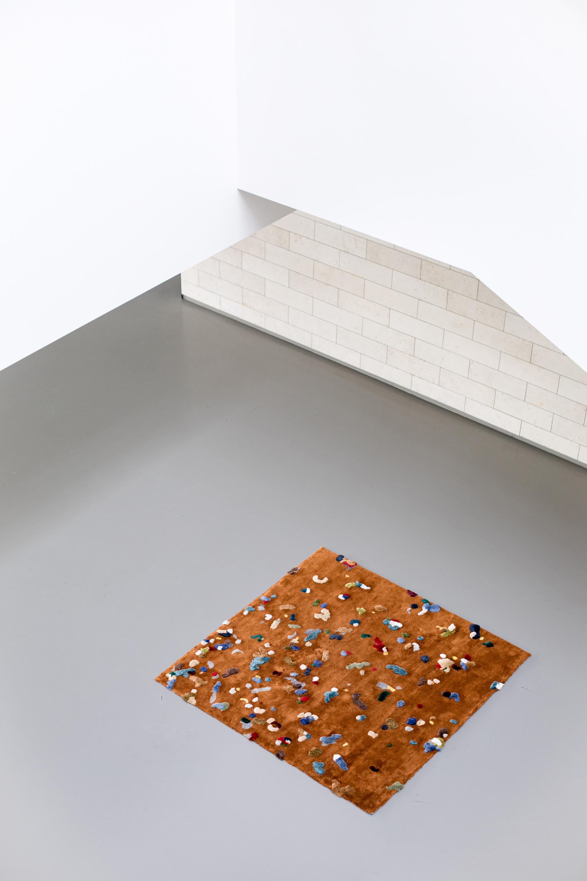 Chaos Rug by Audronė Drungilaitė displayed on a modern floor, featuring a textured brown surface with colorful confetti-like patterns.
