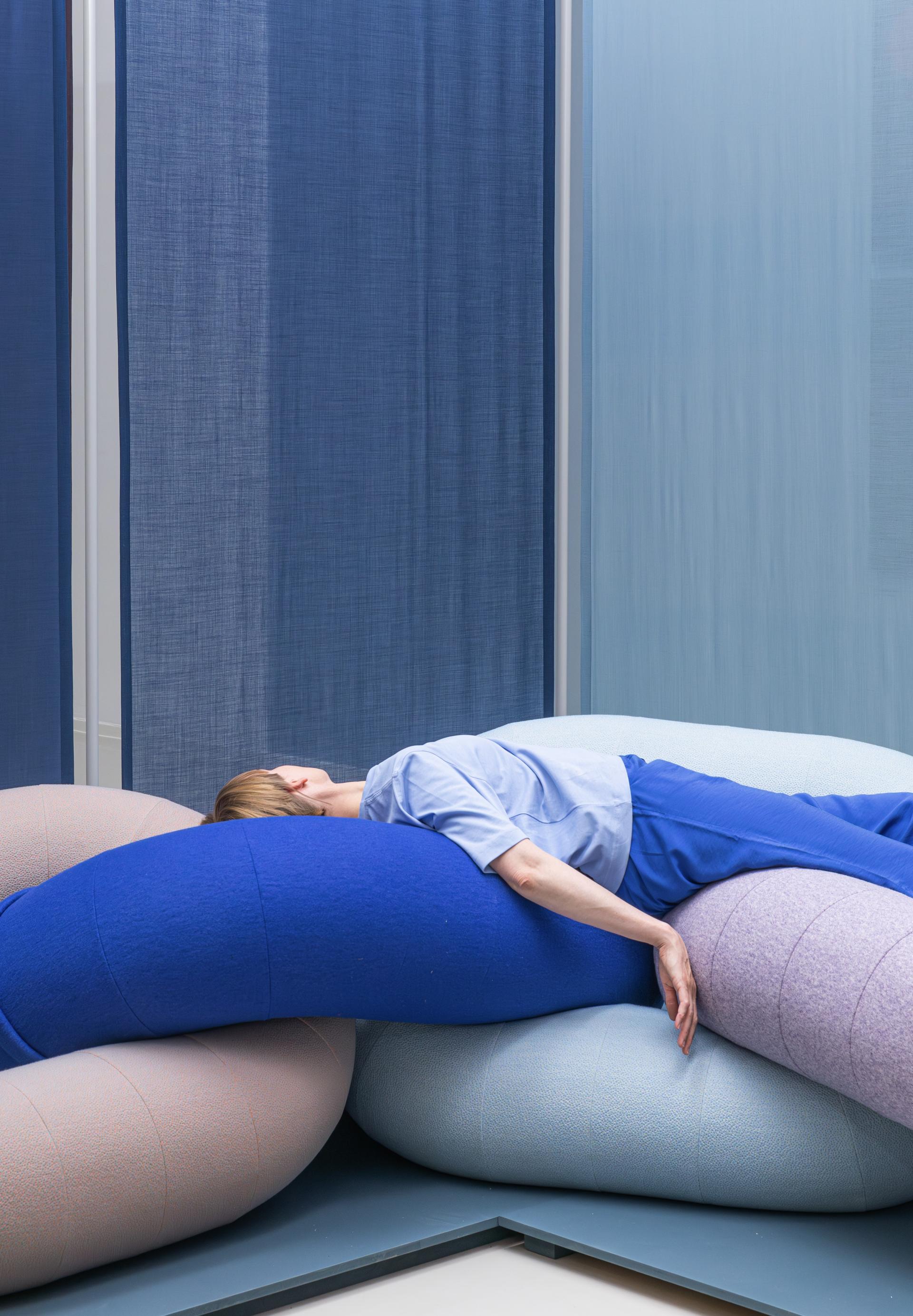 A person reclines on soft, bio-based cushions in a serene, color-coordinated interior space, highlighting material interaction.