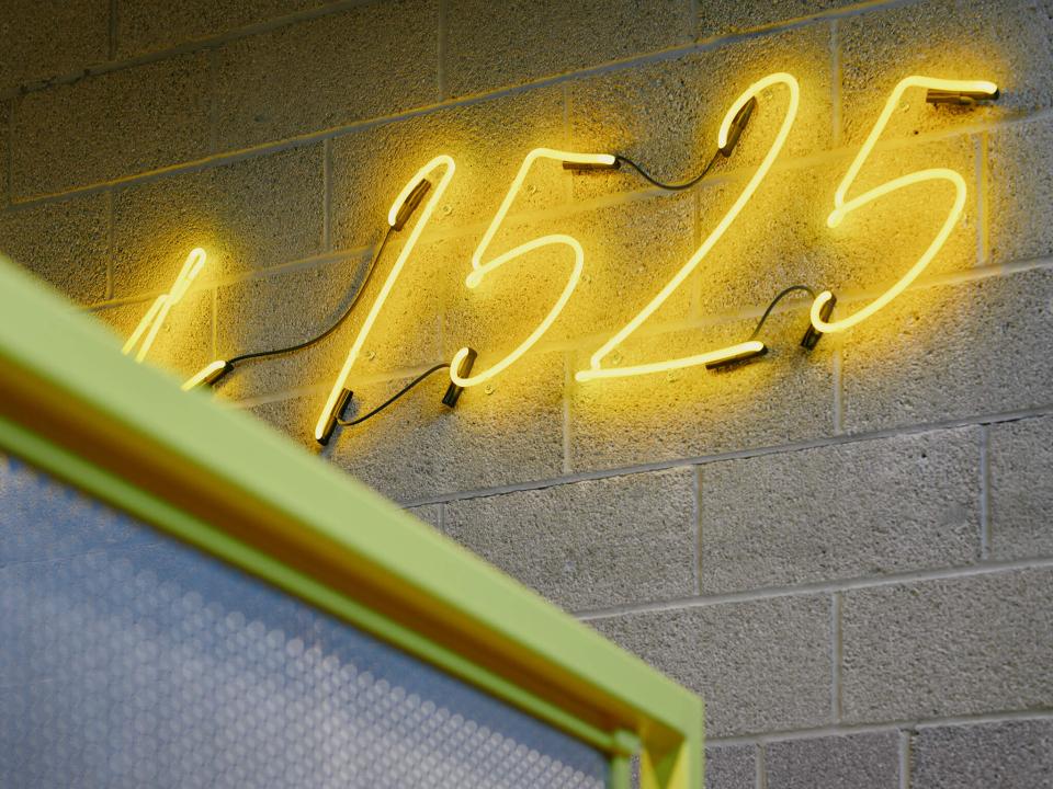 Neon yellow sign displaying "1525" against a textured gray wall, enhancing Sedbergh School's vibrant atmosphere.
