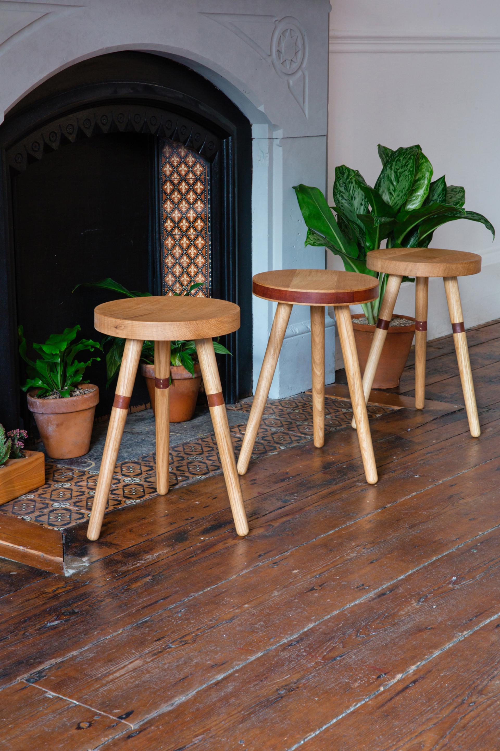 Three handmade wooden stools with natural finishes, positioned near a decorative fireplace and indoor plants.