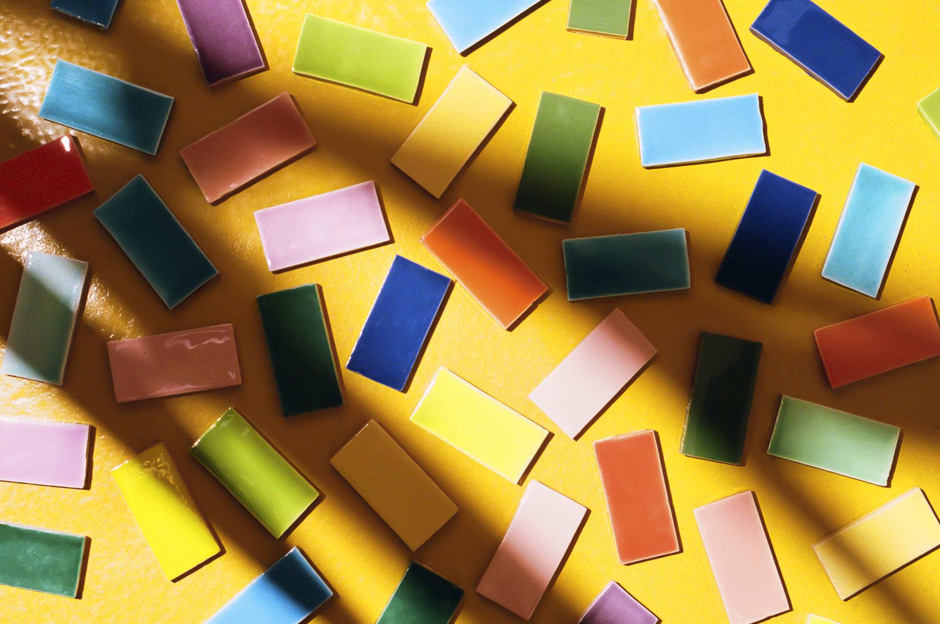 Vibrant technicolour tiles scattered across a yellow surface, showcasing Domus and Yinka Ilori's unique design collaboration.
