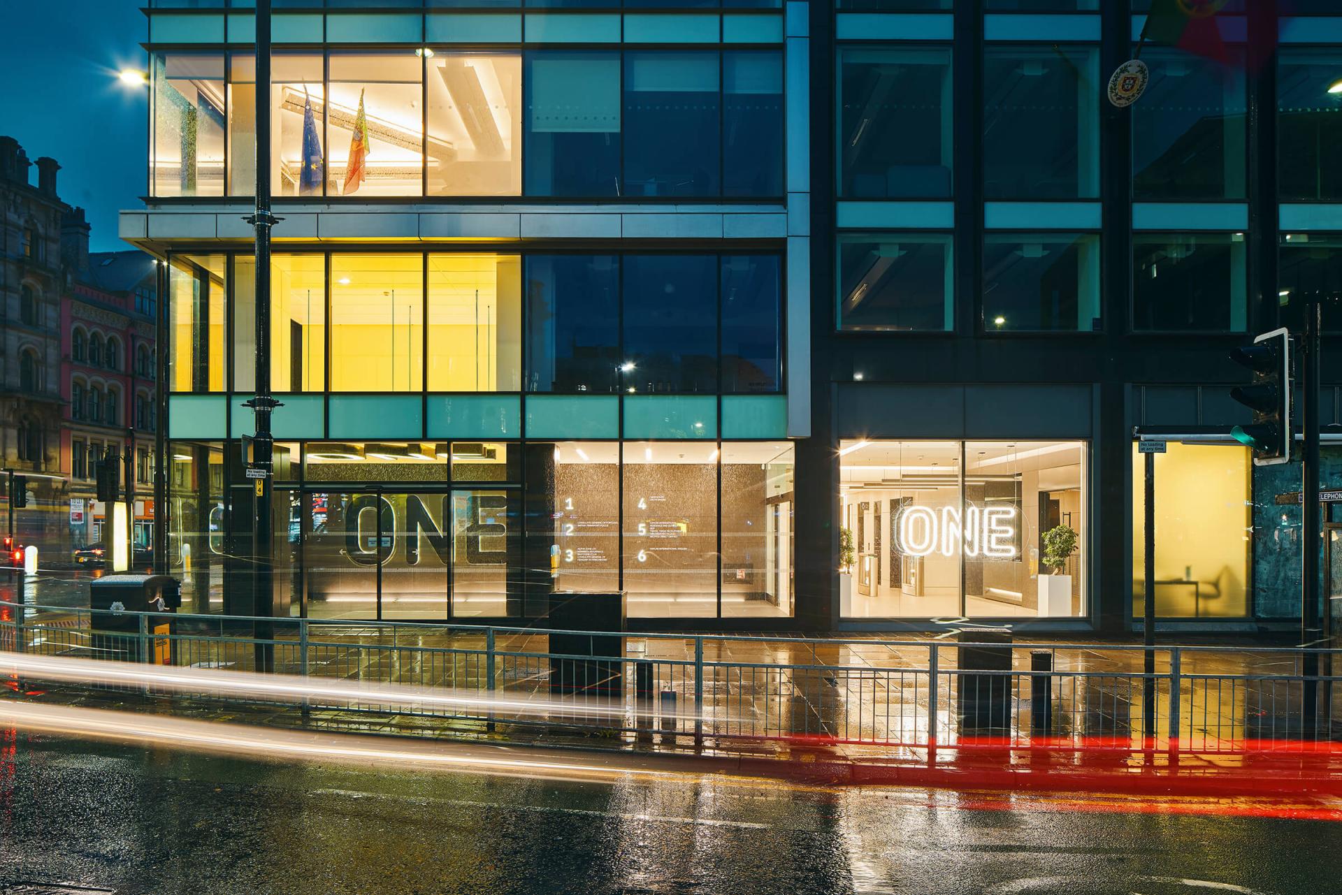 Modern office building at night, featuring illuminated signage and a sleek glass facade, showcasing design innovation.
