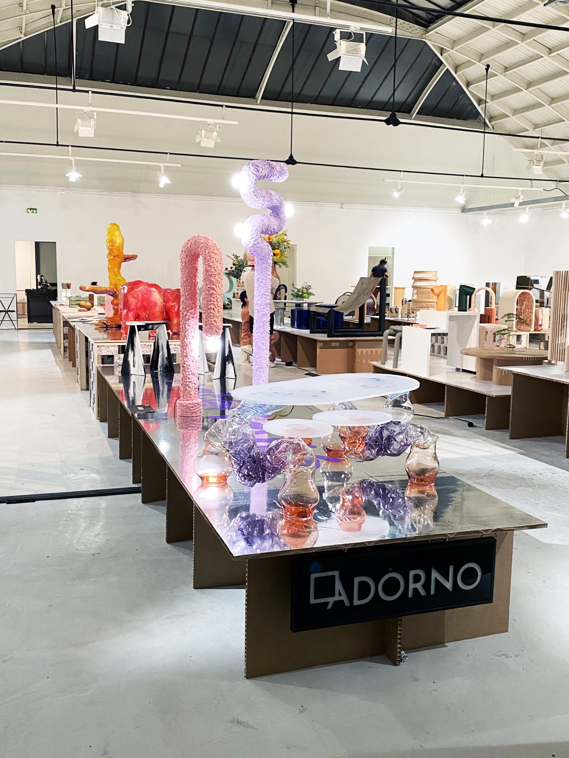 Colorful sculptures and decorative objects displayed on tables at Adorno's Matérialité exhibition during Paris Design Week.