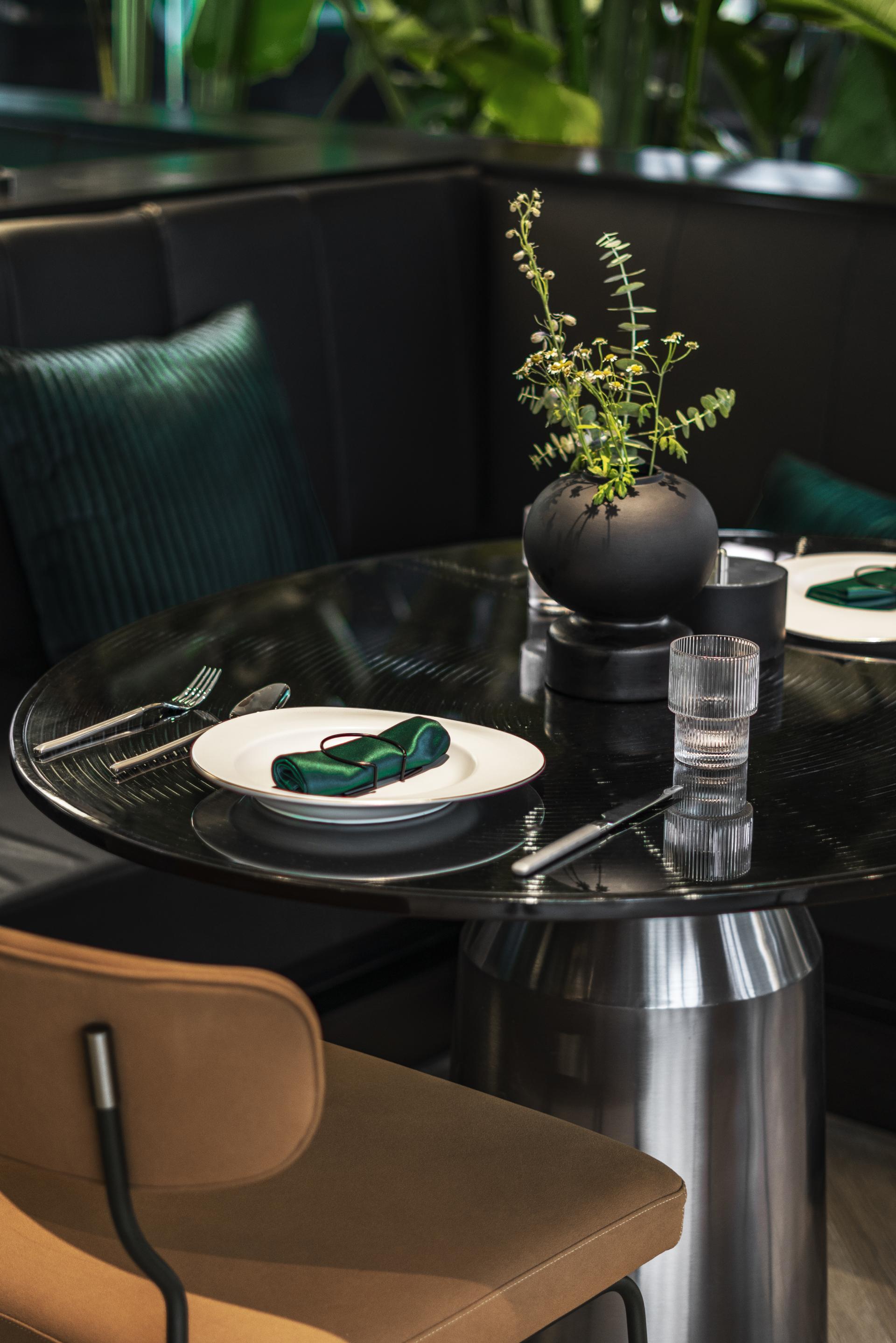 Elegant dining setup featuring a dark wooden table, green accents, and a plant centerpiece in a nature-themed restaurant.