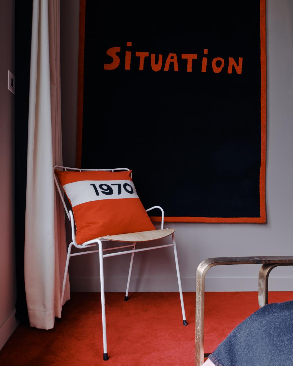 Elegant interior featuring a white chair with an orange cushion, against a bold black wall tapestry saying 