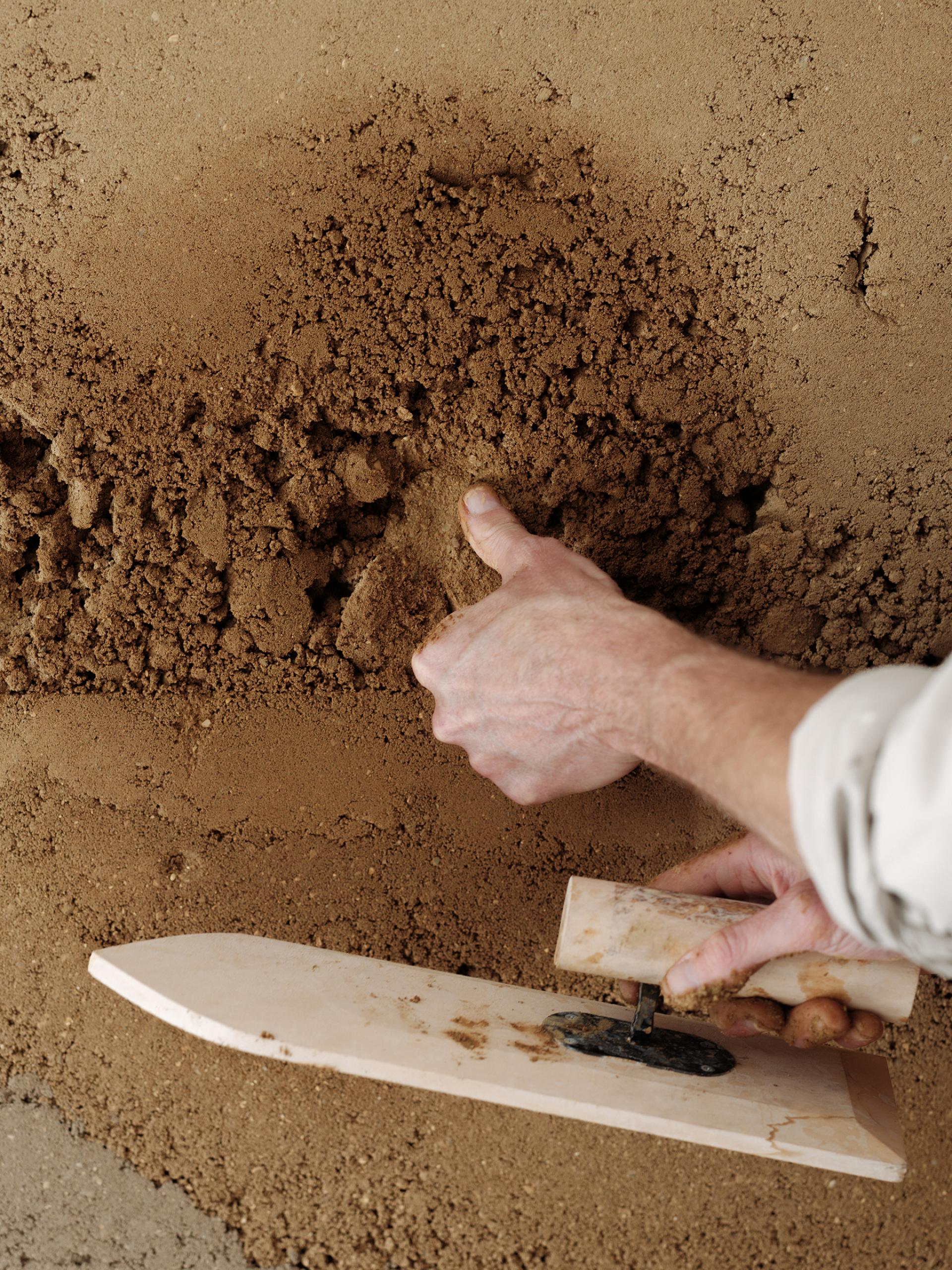 Hands expertly applying a natural clay wall finish, showcasing the sustainable craftsmanship of Clayworks' Rammed Earth range.