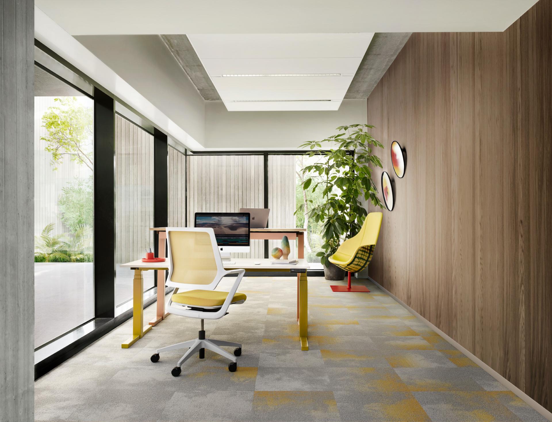 Modern office workspace featuring a minimalist design with yellow accents, glass walls, and greenery for a vibrant atmosphere.