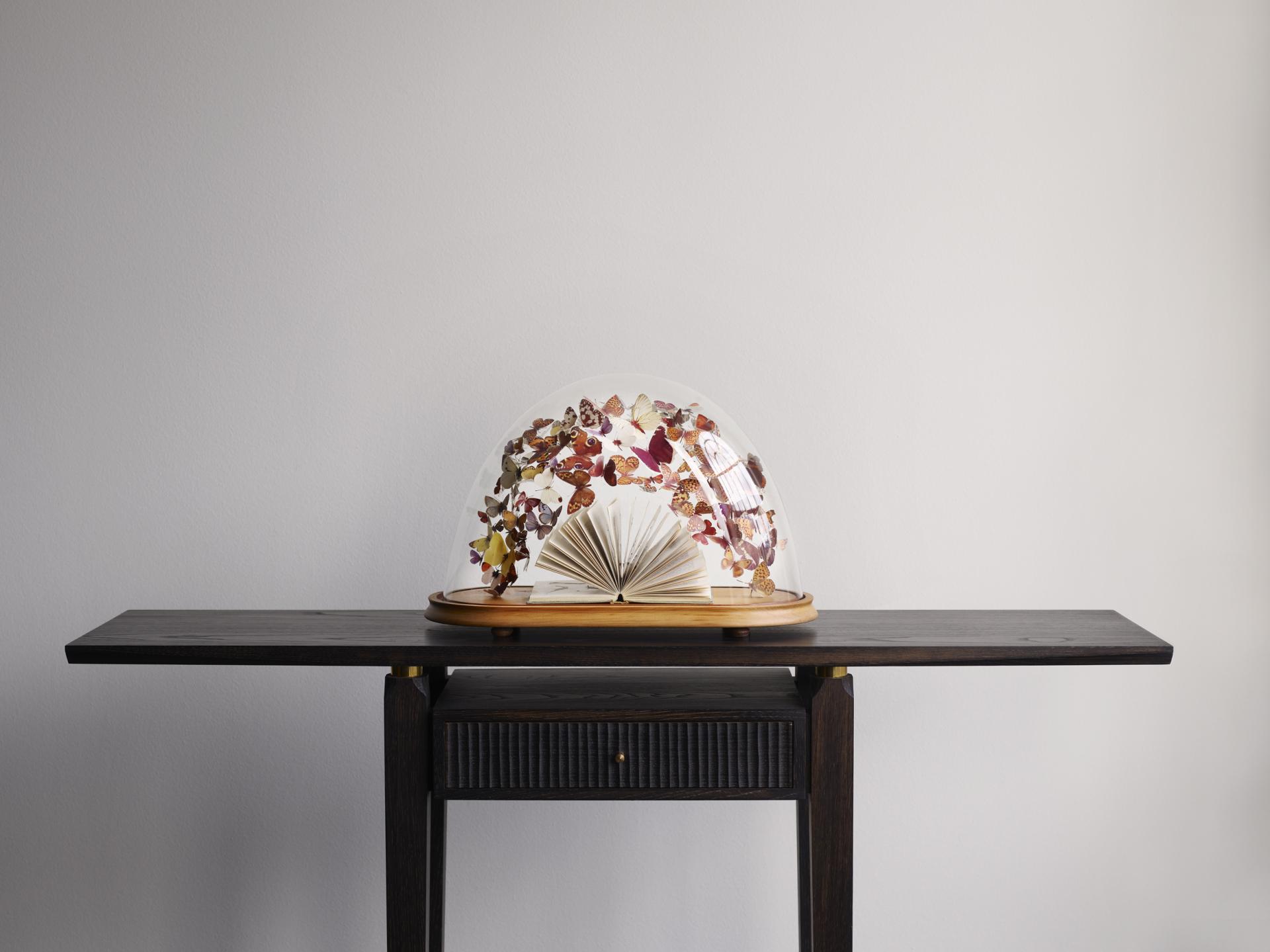 A unique display featuring a preserved book under a glass dome adorned with colorful dried flowers and butterflies.