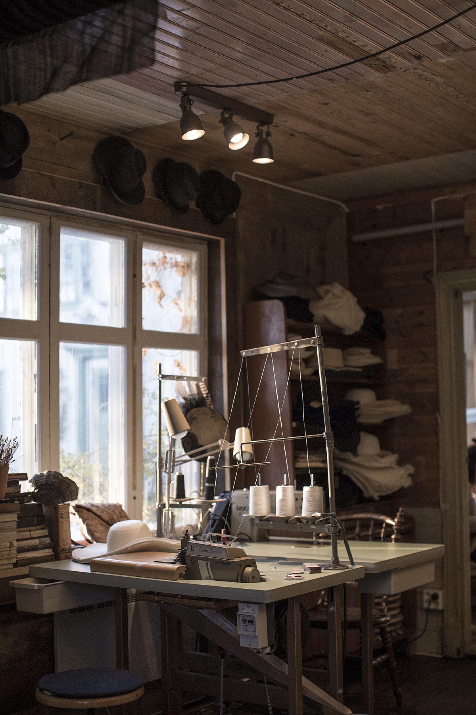 Workshop interior of Horisaki in Småland, featuring sewing machines, hat materials, and natural light filtering through windows.
