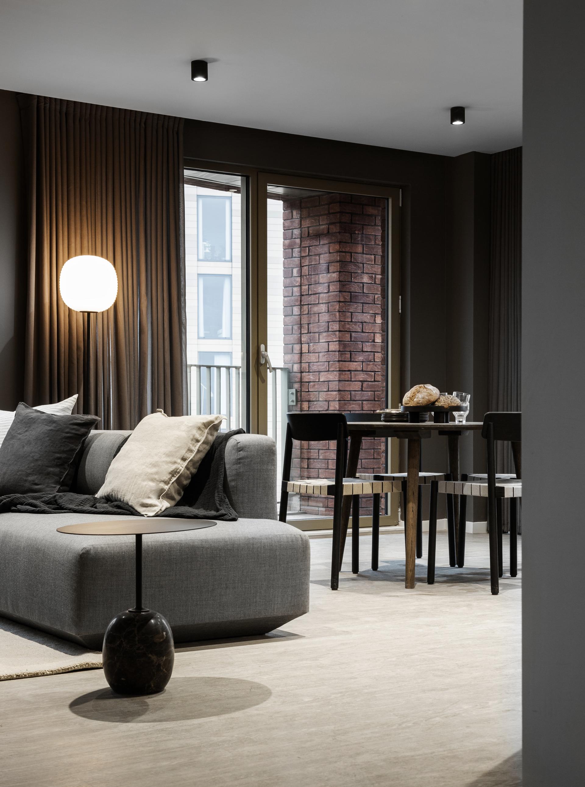 Modern living room in Manchester featuring a cozy gray sofa, dining area, and large windows with natural light.