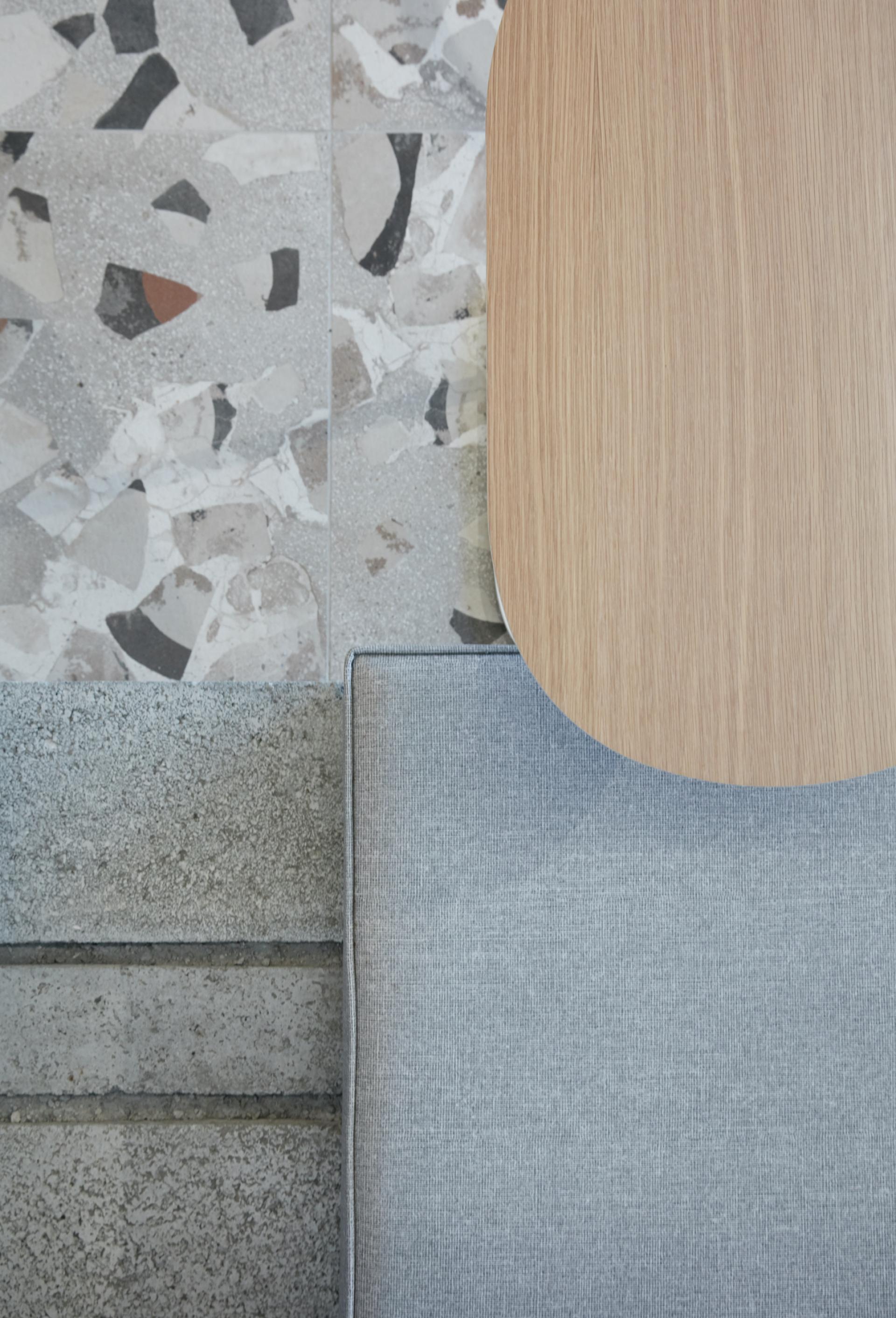Stylish minimalist interior featuring a wooden tabletop, grey fabric seating, and textured terrazzo flooring in a Dubai coffee shop.