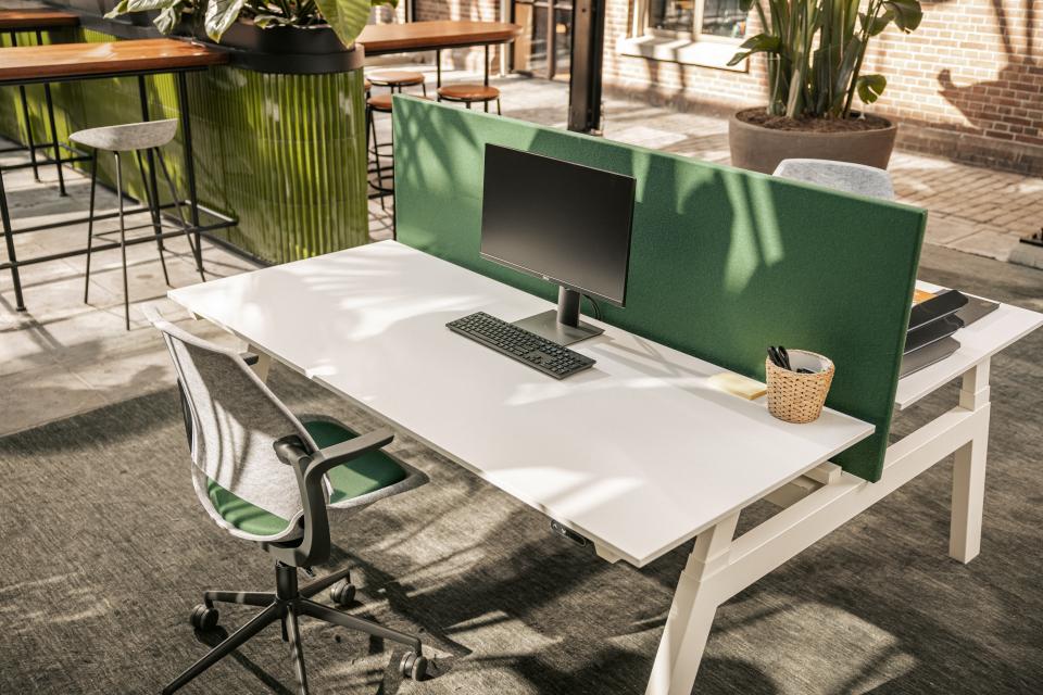 Modern office workspace featuring Vepa's Be Hybrid task chair, a computer setup, and a green acoustic panel for privacy.