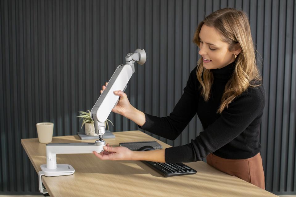 A woman adjusts a Rising™ monitor arm on a desk, showcasing its adaptable design for inclusive workspaces.