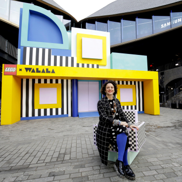 Camille Walala poses in front of her colorful HOUSE OF DOTS installation with LEGO at Coal Drops Yard, London.