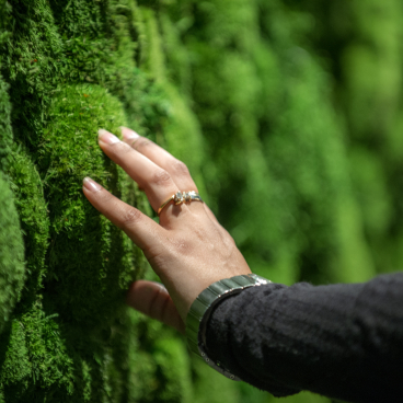 A hand gently touches a vibrant green moss wall, highlighting innovative surface design at the Surface Design Show.