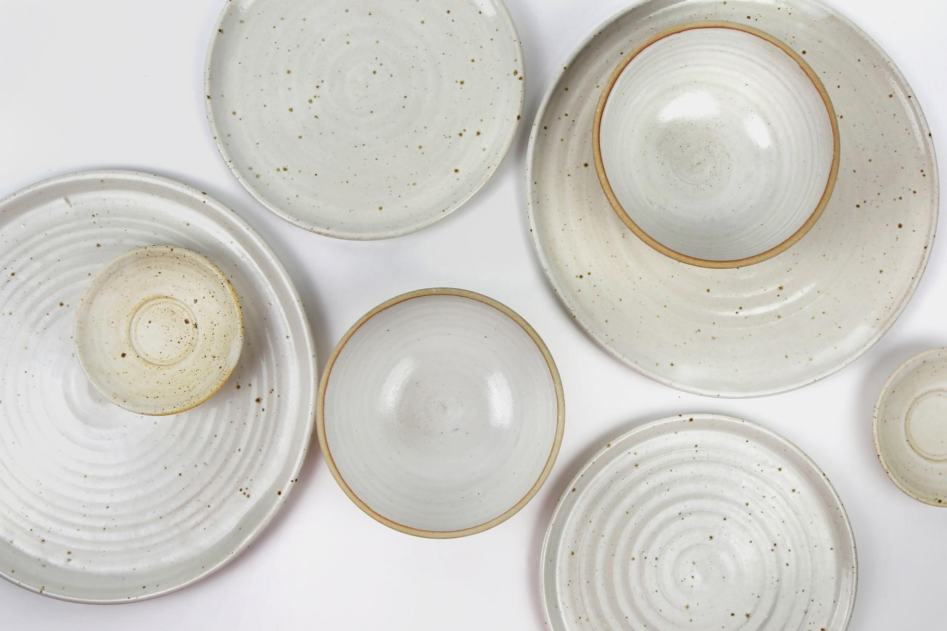 Handcrafted ceramic bowls and plates in various sizes, showcasing a rustic white glaze and subtle speckled textures.