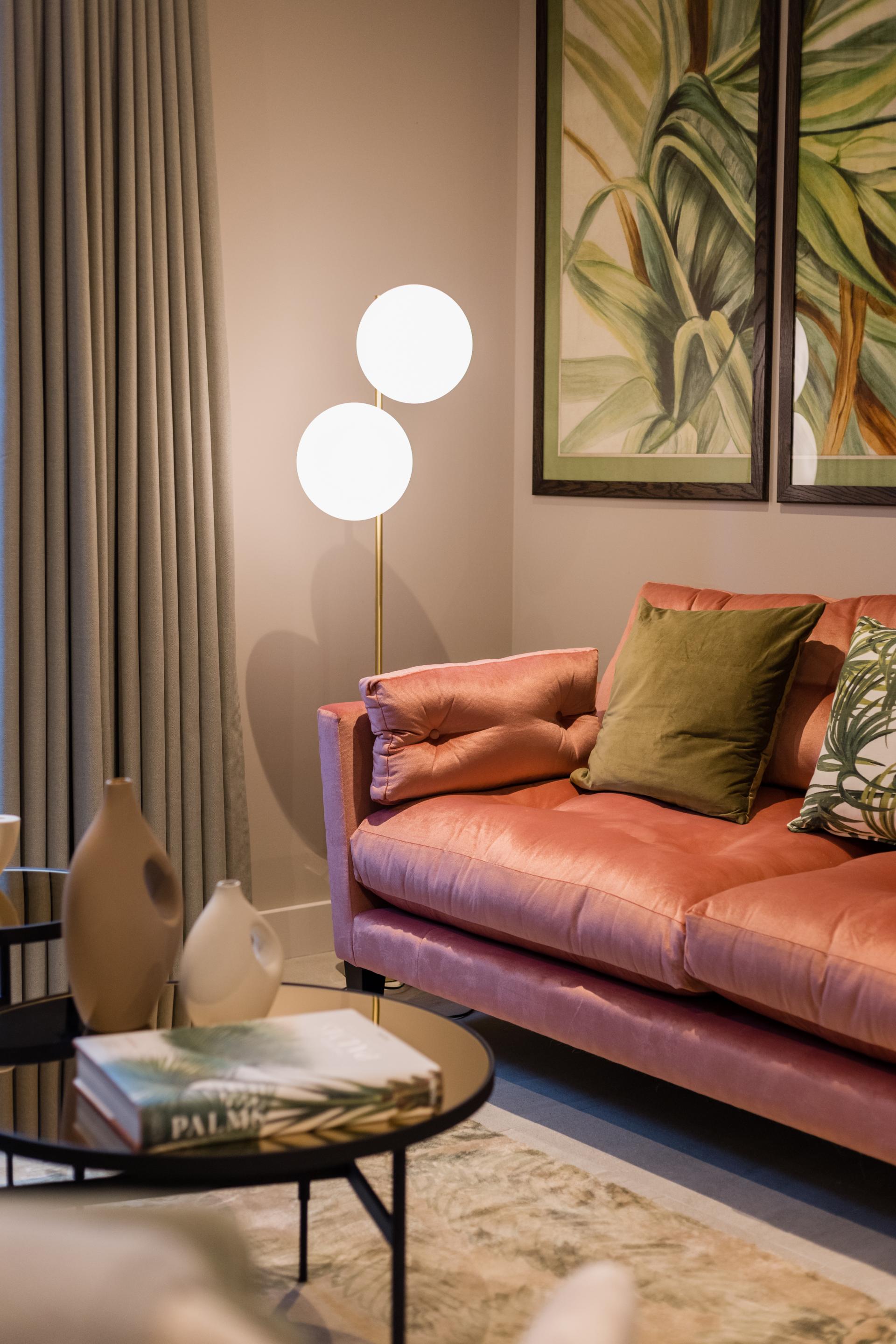 Stylish living room featuring a pink sofa with green pillows, modern lamp, and decorative coffee table, highlighting rental design trends.