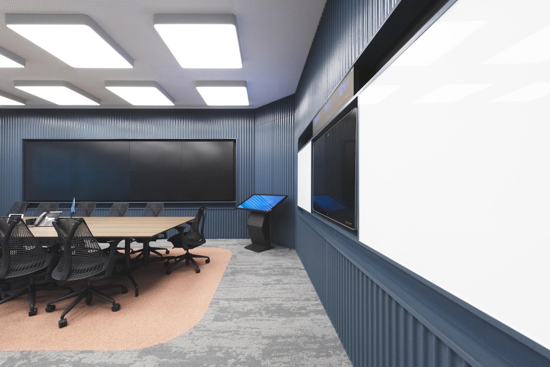 Modern conference room designed by Bean Buro, featuring a large table, ergonomic chairs, and digital displays on the walls.