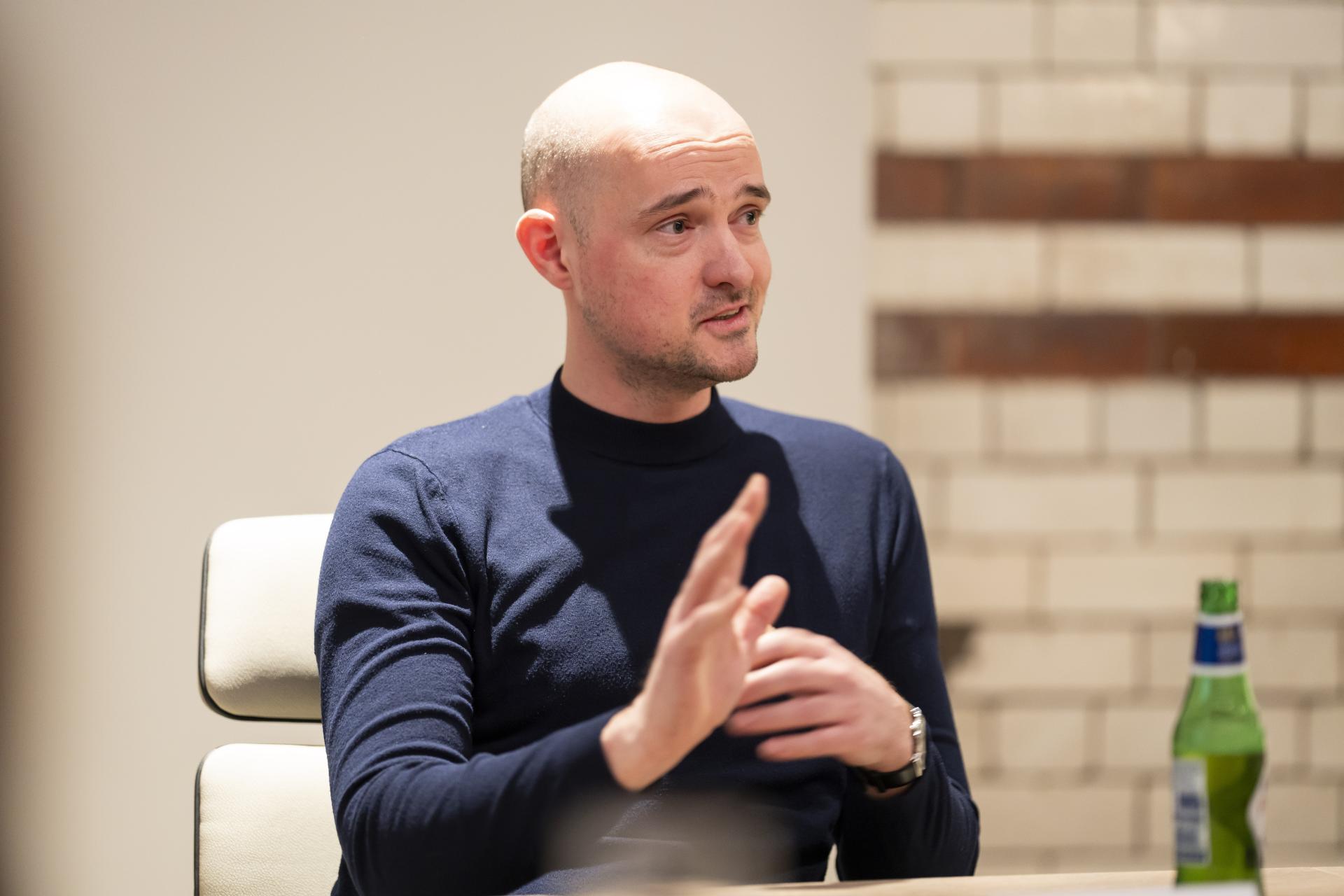 Engaged speaker discussing technology's role in sustainable design during a collaborative meeting, with a beverage on the table.