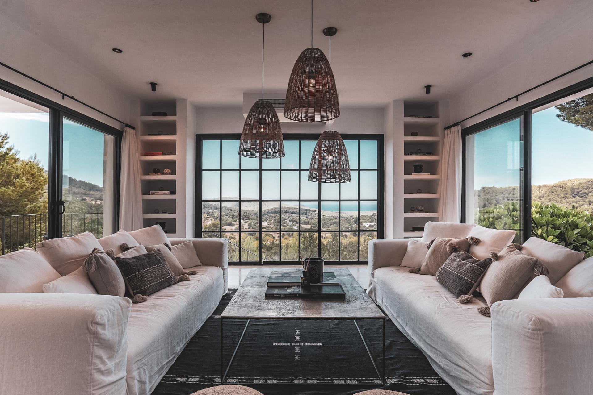 Stylish living room showcasing elegant white sofas, decorative pillows, and panoramic views of nature, reflecting modern interior design aesthetics.