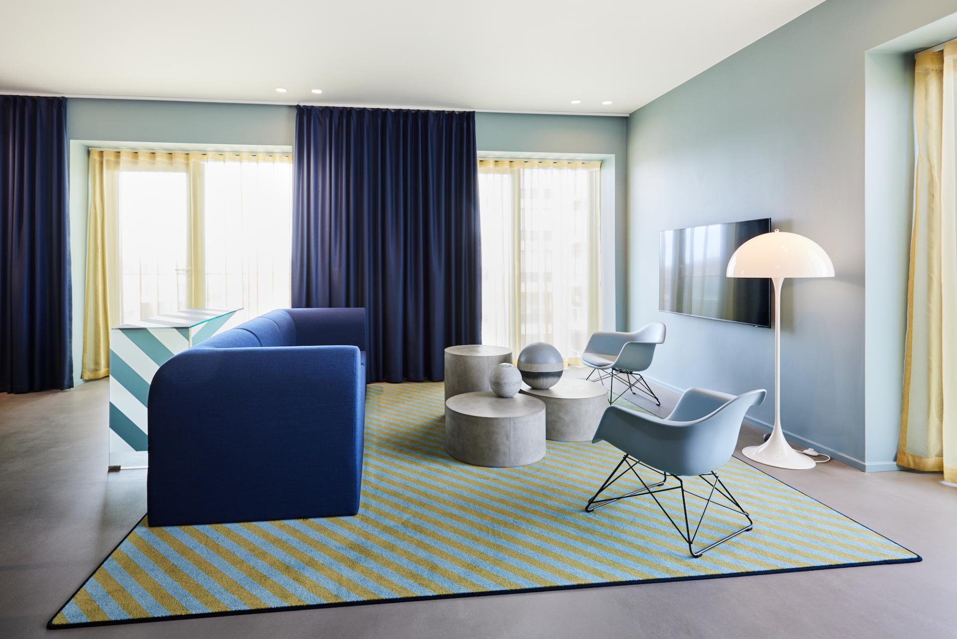 Vibrant lounge area at Kirk Suites featuring blue striped rug, modern furniture, and large windows with natural light.