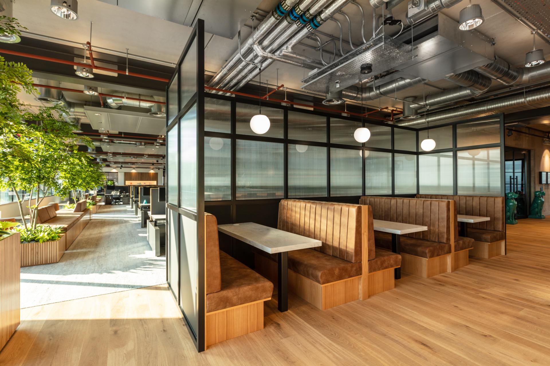 Modern office interior featuring cozy seating booths, greenery, and natural light, designed for collaboration at Alpha FX London.