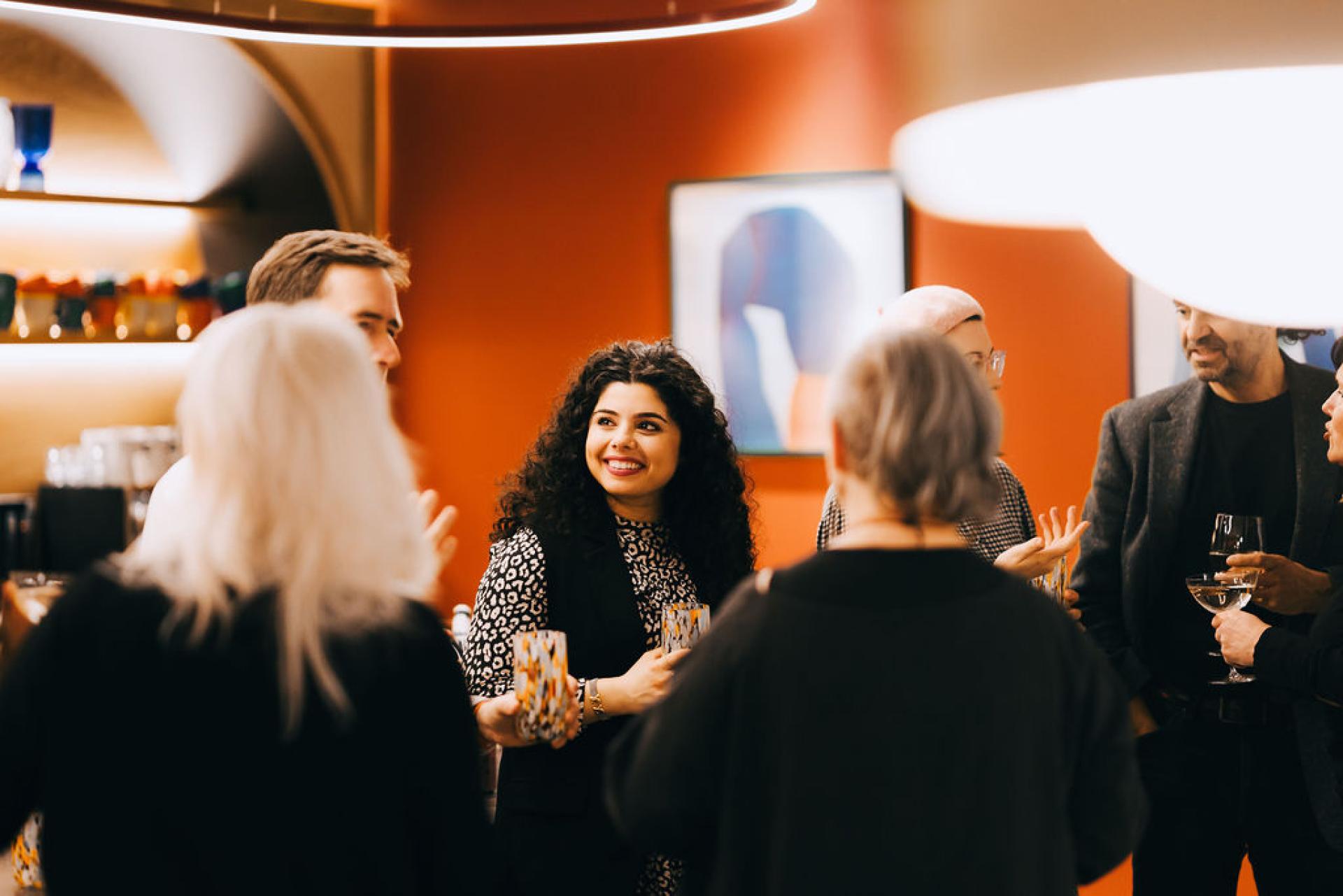 A diverse group of people engaging in conversation at a sustainability-focused event, holding drinks in a vibrant setting.