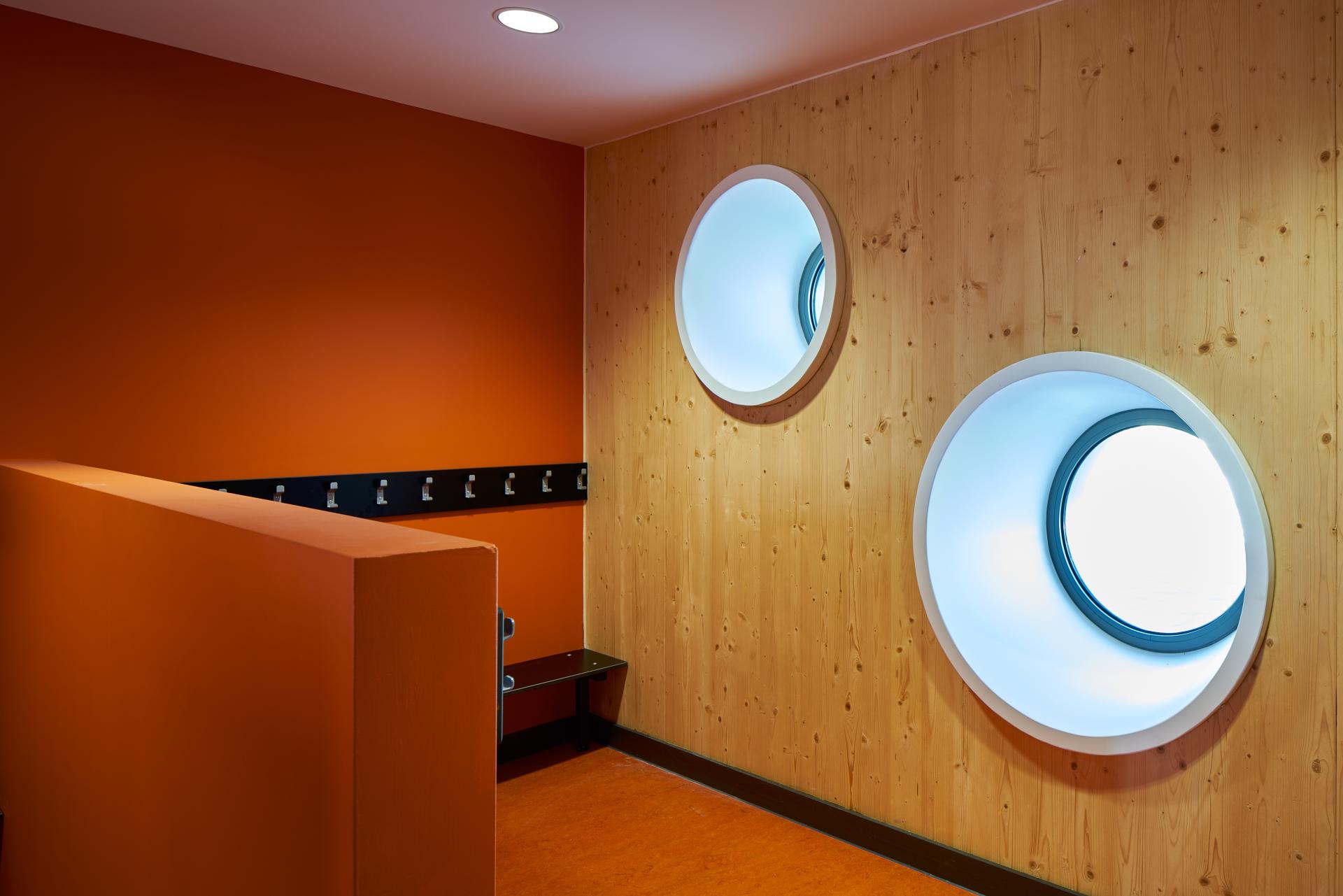 Brightly colored interior space featuring circular windows, showcasing innovative use of cross-laminated timber design elements.