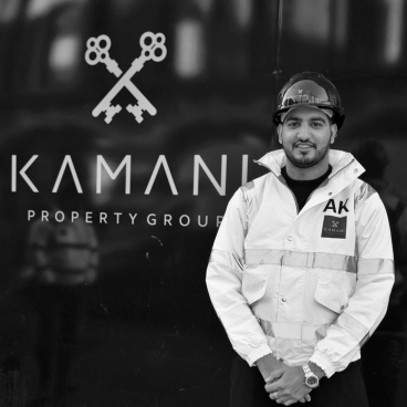 Adam Kamani, CEO of Kamani Property Group, stands confidently in front of the company logo in Manchester.