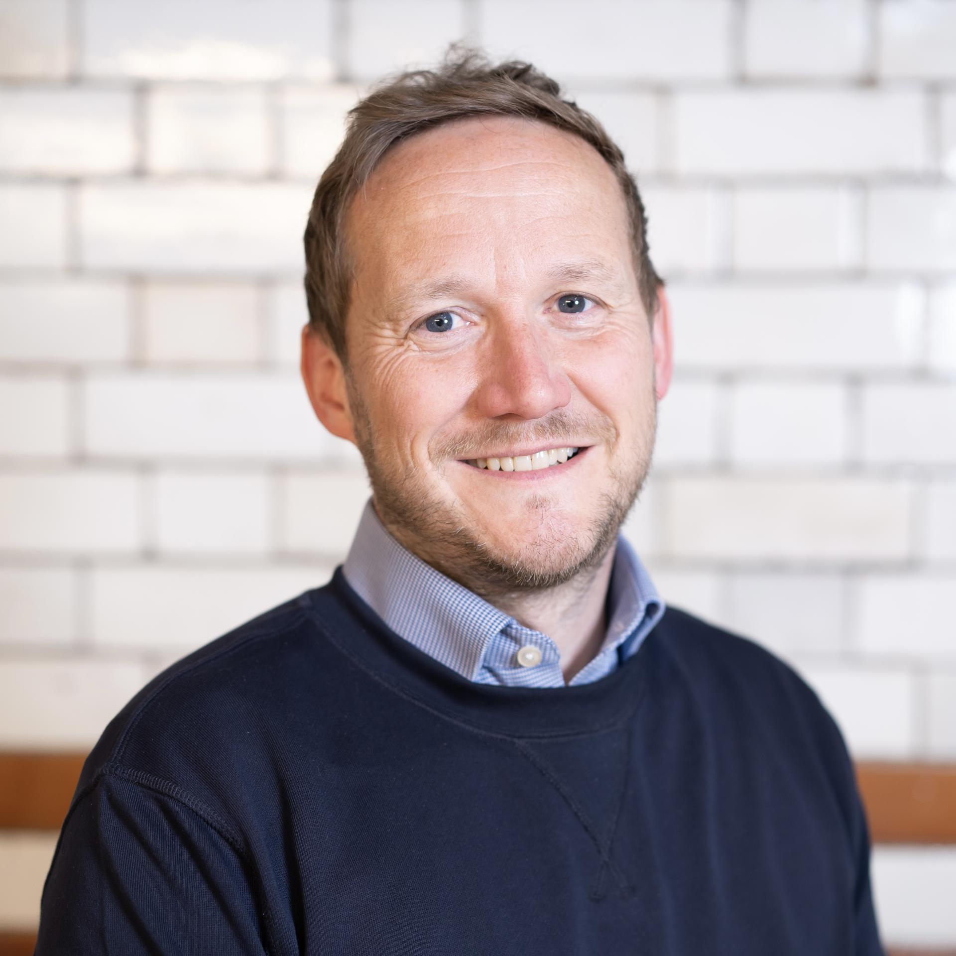 Smiling man in a casual sweater representing the professional atmosphere of a technologically advanced workplace.