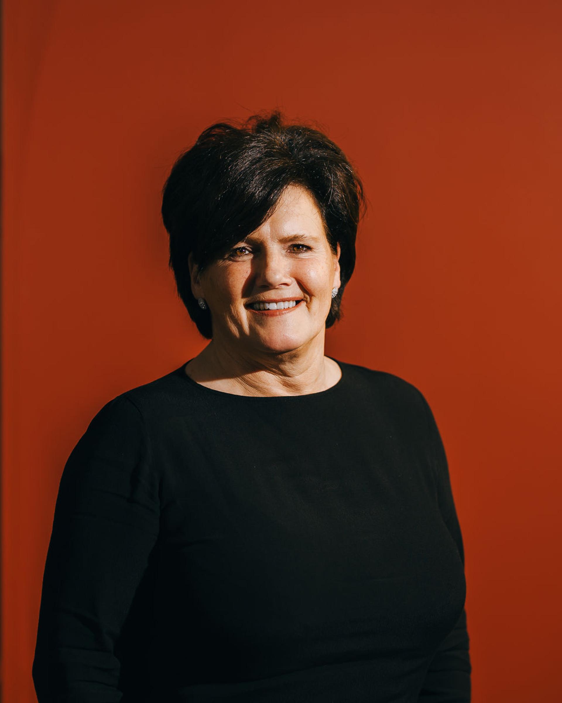 Smiling woman in a black shirt poses against a vibrant red background, highlighting themes of sustainability in biomaterials.