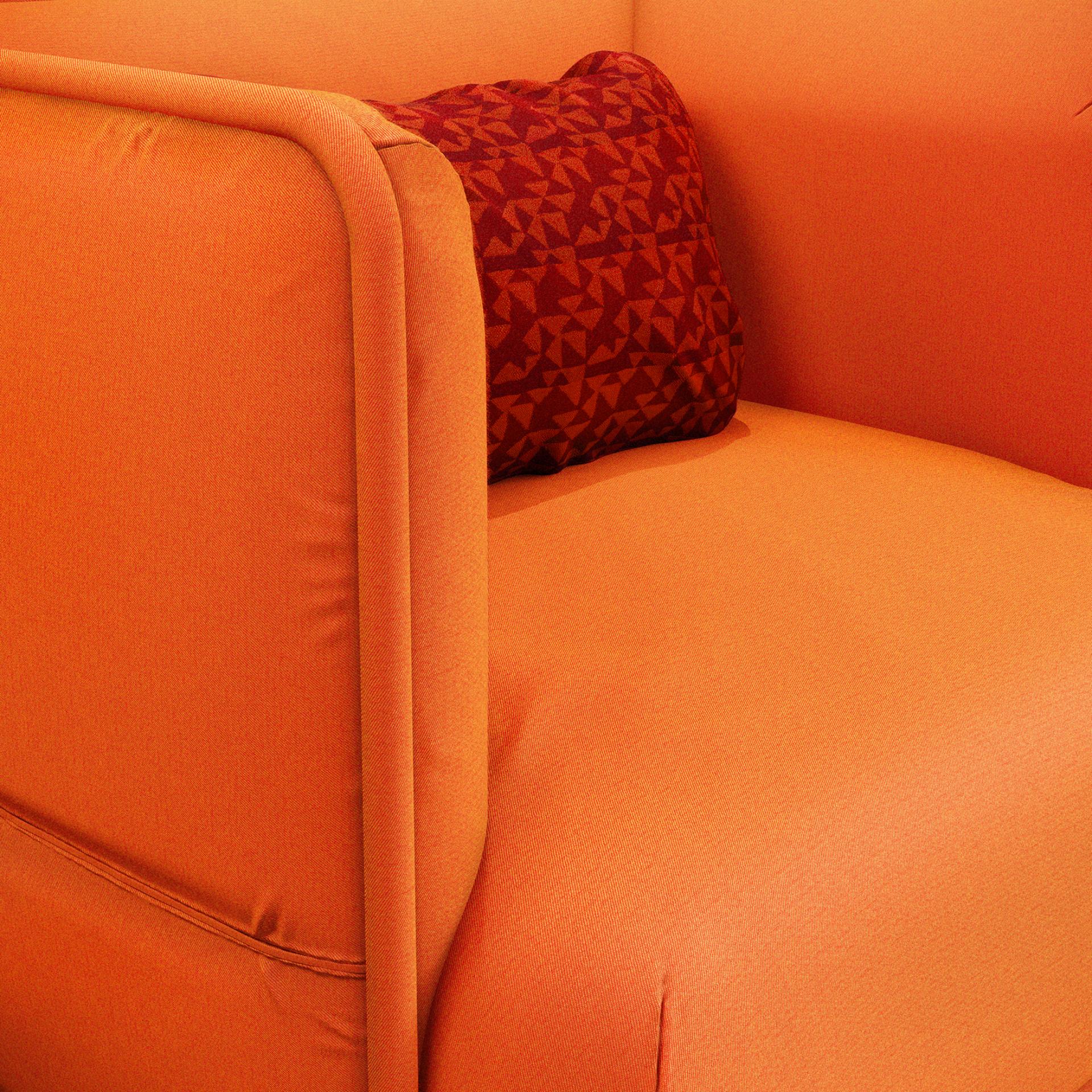 Vibrant orange upholstery of a modern sofa, featuring a decorative red patterned pillow, highlighting color and comfort in design.